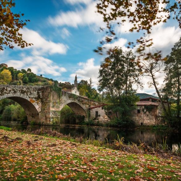 Fall foliage and medieval Roman bridge reflected on the water in the Galician village of Allariz, Ourense.